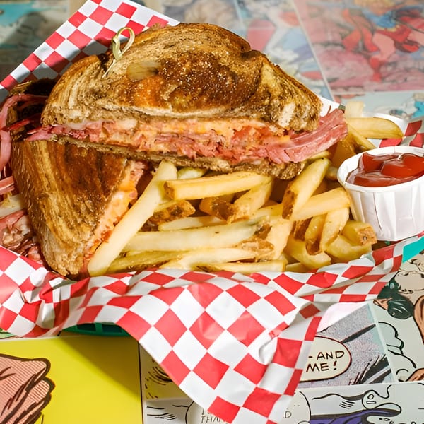 A pastrami sandwich and fries with ketchup in a red and white checkered basket.