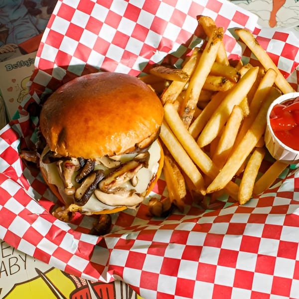 Mushroom burger and french fries with ketchup in a red and white checkered paper-lined basket.