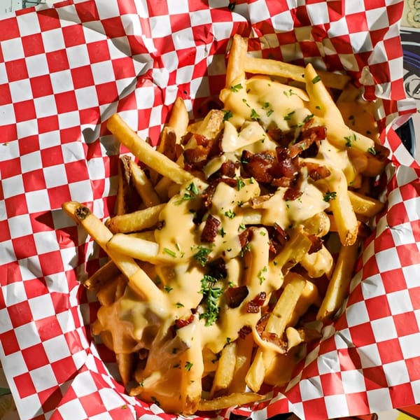 Golden french fries topped with melted cheese, crispy bacon bits, and fresh parsley in a red and white checkered basket.