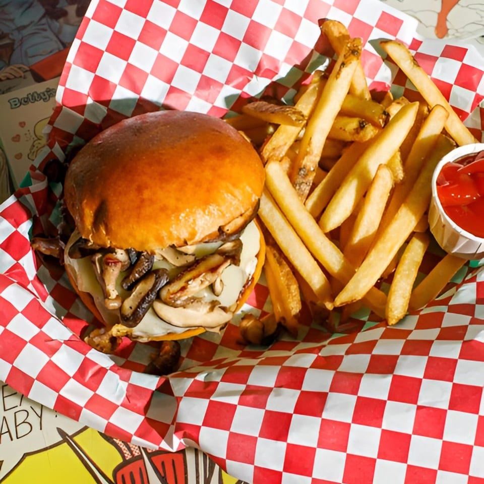 Mushroom Swiss burger and golden fries with ketchup in a red and white checkered basket.