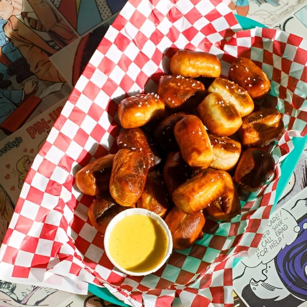A basket of pretzel bites with salt and a side of mustard, on a comic book background.