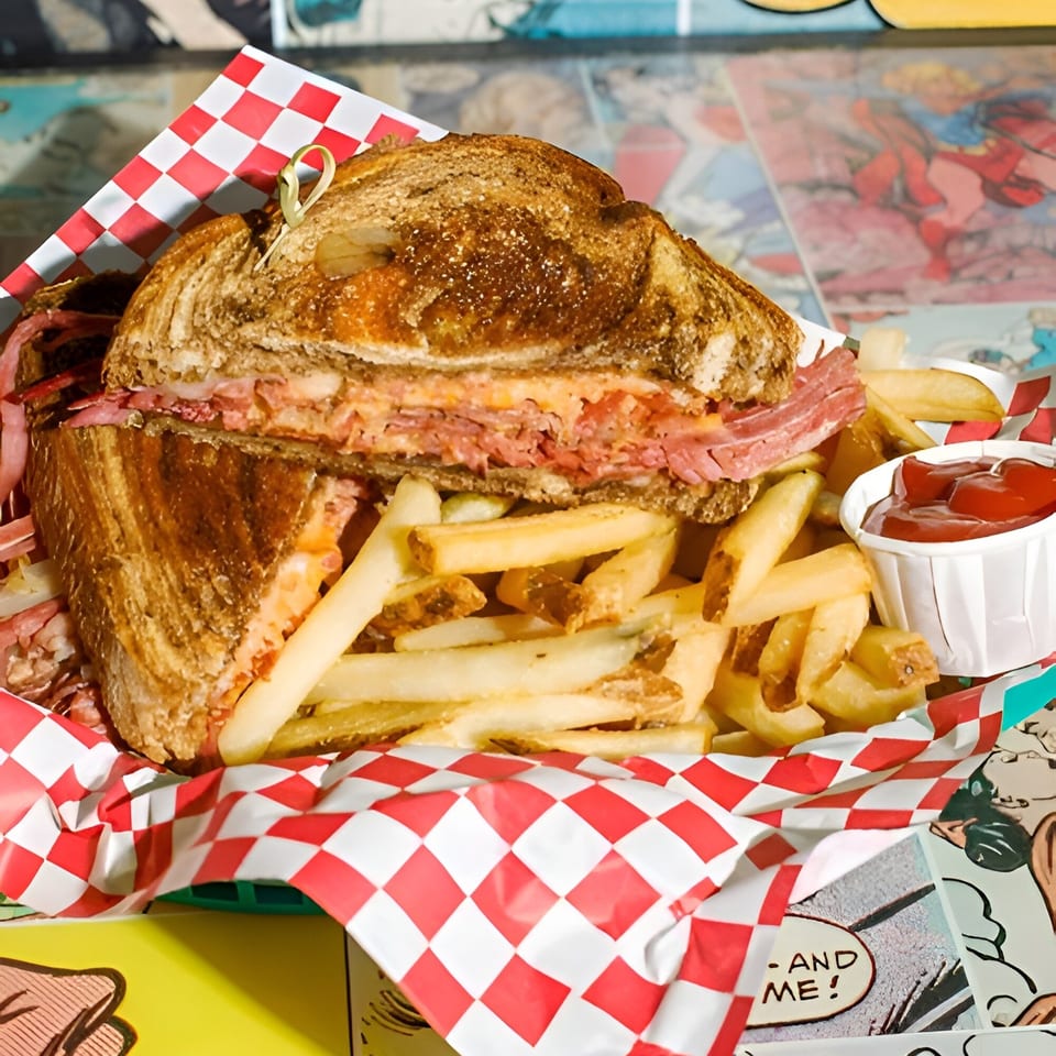 A hearty pastrami sandwich with melted cheese and fries in a red and white checkered basket.