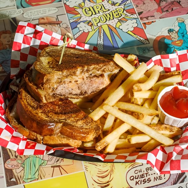 A patty melt with fries and ketchup in a red and white checkered basket on a comic book background.
