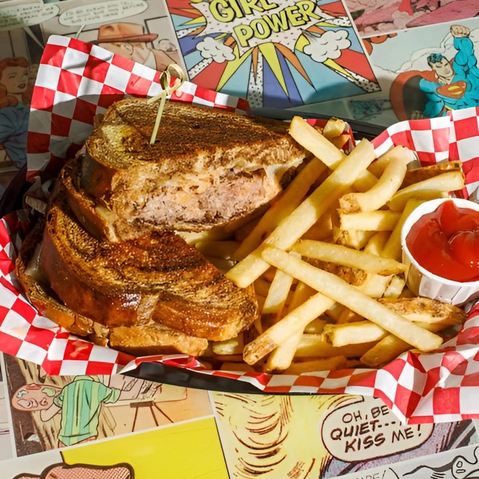 A grilled sandwich and fries with ketchup in a red and white checkered basket on a comic book background.