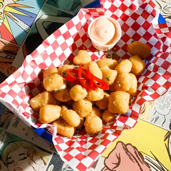 Fried cheese curds with red pepper slices and dipping sauce in a red and white checkered basket.