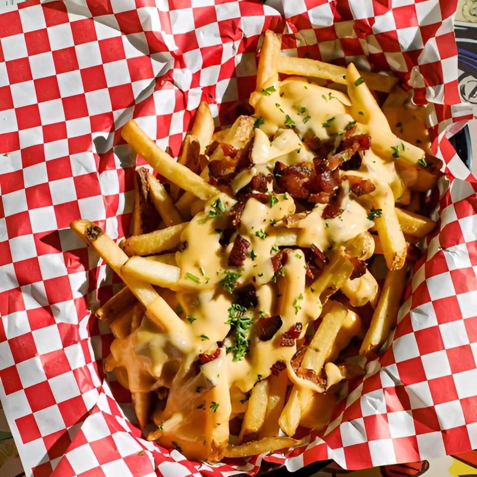 Golden french fries covered in melted cheese, crispy bacon bits, and fresh parsley in a red and white checkered basket.