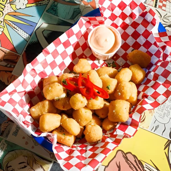 Golden fried cheese curds with sliced red chilies and a side of dipping sauce in a red checkered basket.