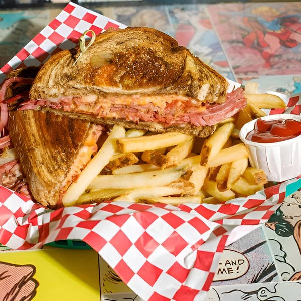 A pastrami sandwich, cut in half, with fries and ketchup in a red and white checkered basket.